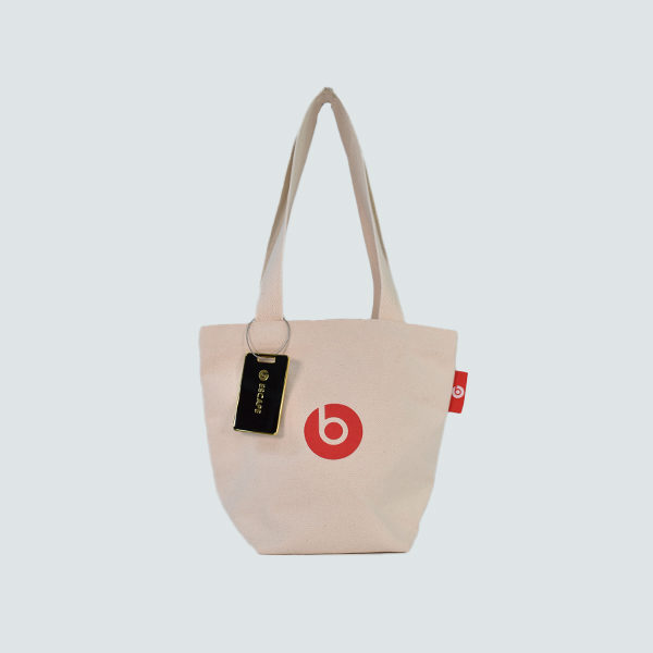 Natural colour tote bag with red logo print and metal luggage tag attached to handle